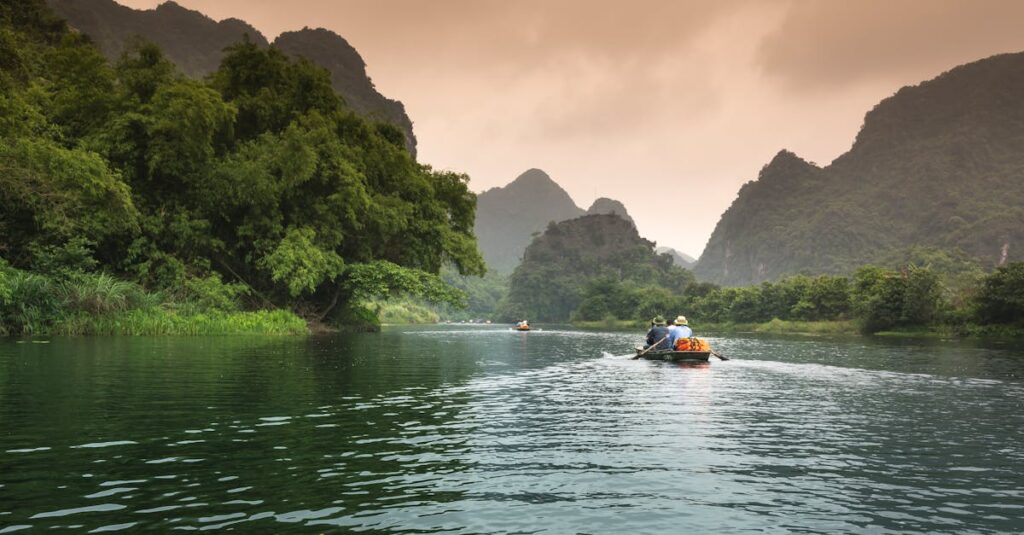 Two people rowing a boat through a serene river surrounded by lush greenery and mountains.